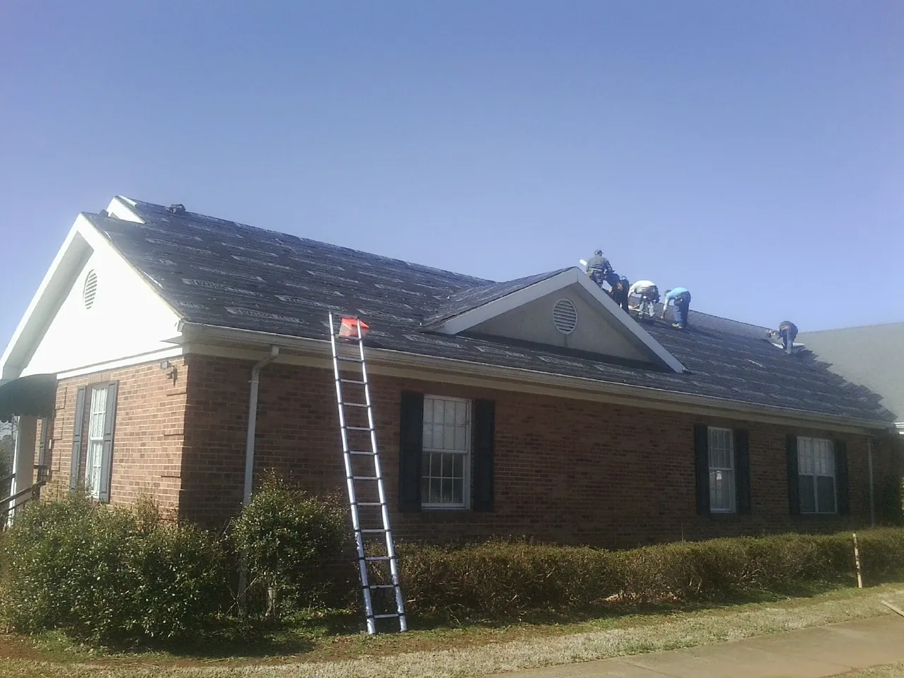 Crew tearing shingles off a brick ranch roof with a ladder set — Metal Roof Repair work by our crew in Hitchcock