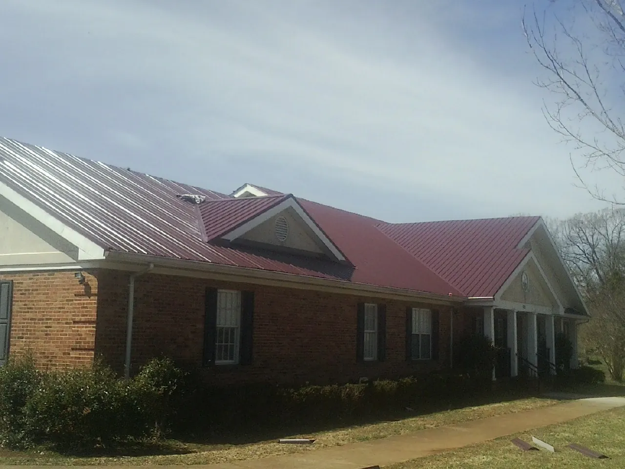 Red metal roof with gabled entries on a long brick building, from a Hail Damage Roof Repair job in Hitchcock