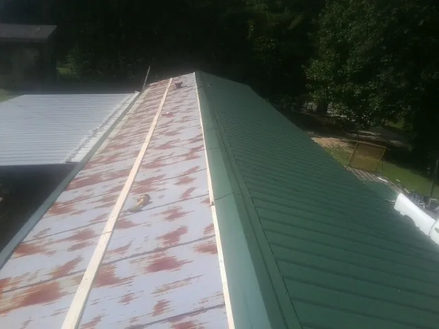 Old rusted panels beside newly installed green metal roofing — Wind Damage Roof Repair by Roofing Brothers in Hitchcock