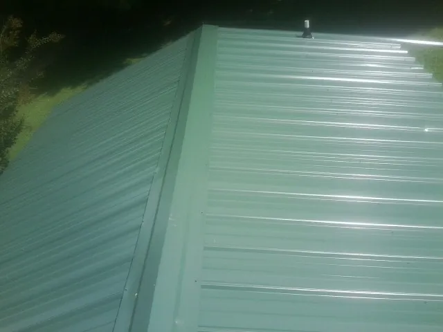New green metal panels meeting at the ridge of a roof — Flat Roof Repair work by our crew in Hitchcock