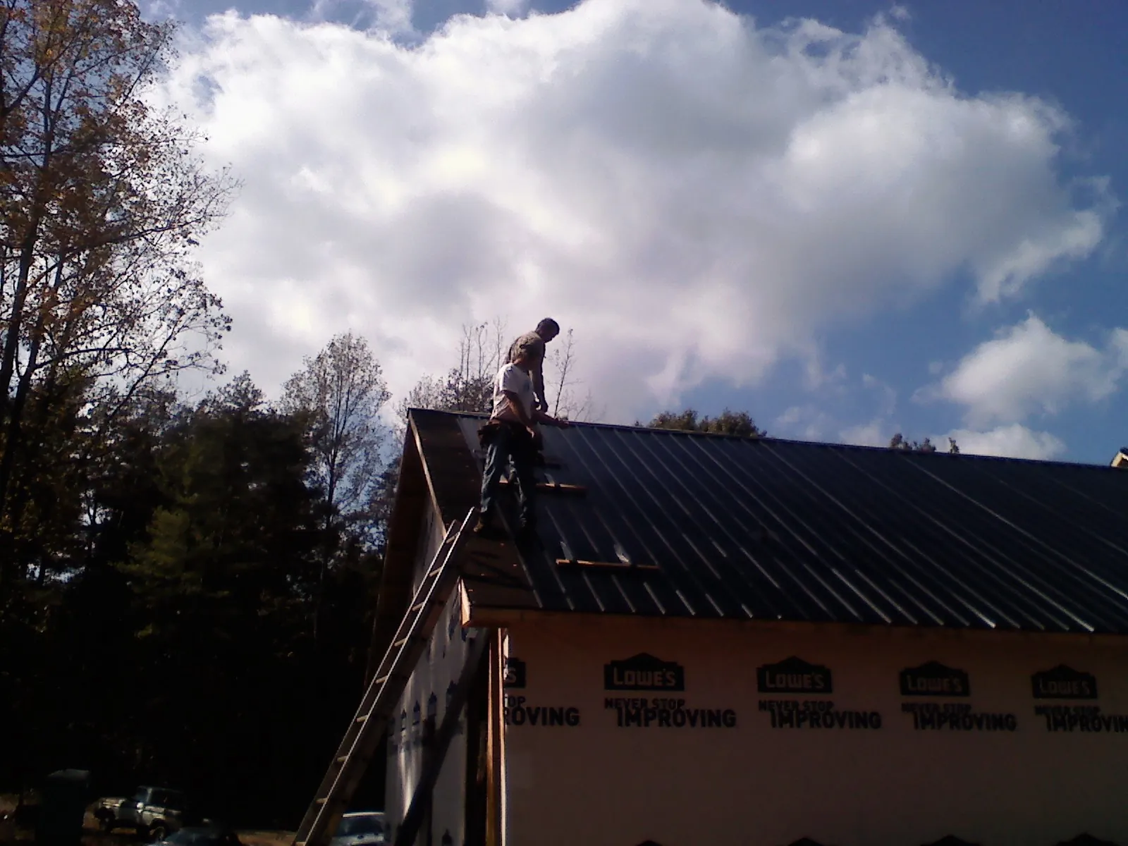 Roofer fastening dark metal panels high against a cloudy sky, from a Roof Inspection job in Hitchcock