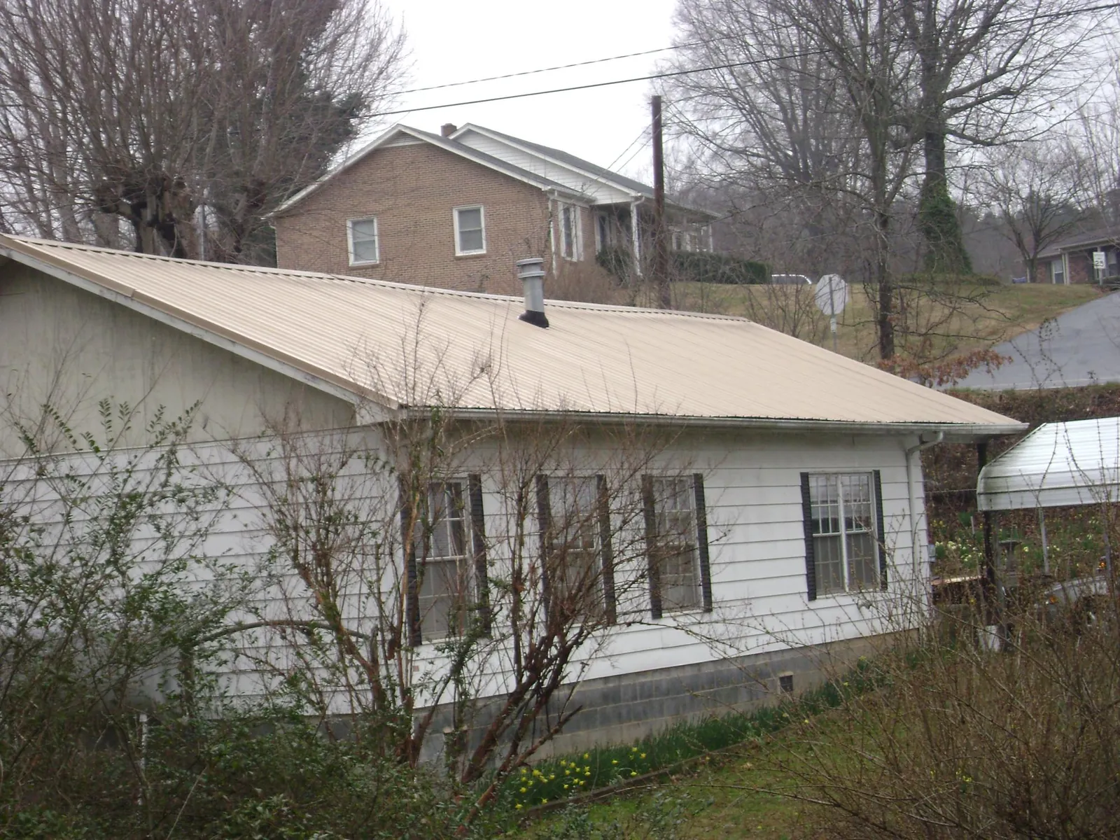 Tan metal roof on a white sided house set into a hillside — Commercial Roofing by Roofing Brothers in Hitchcock