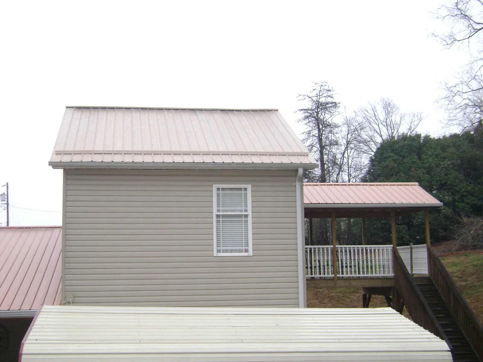 Tan metal roofs on a two story addition and attached porch, from a Roof Replacement job in Hitchcock